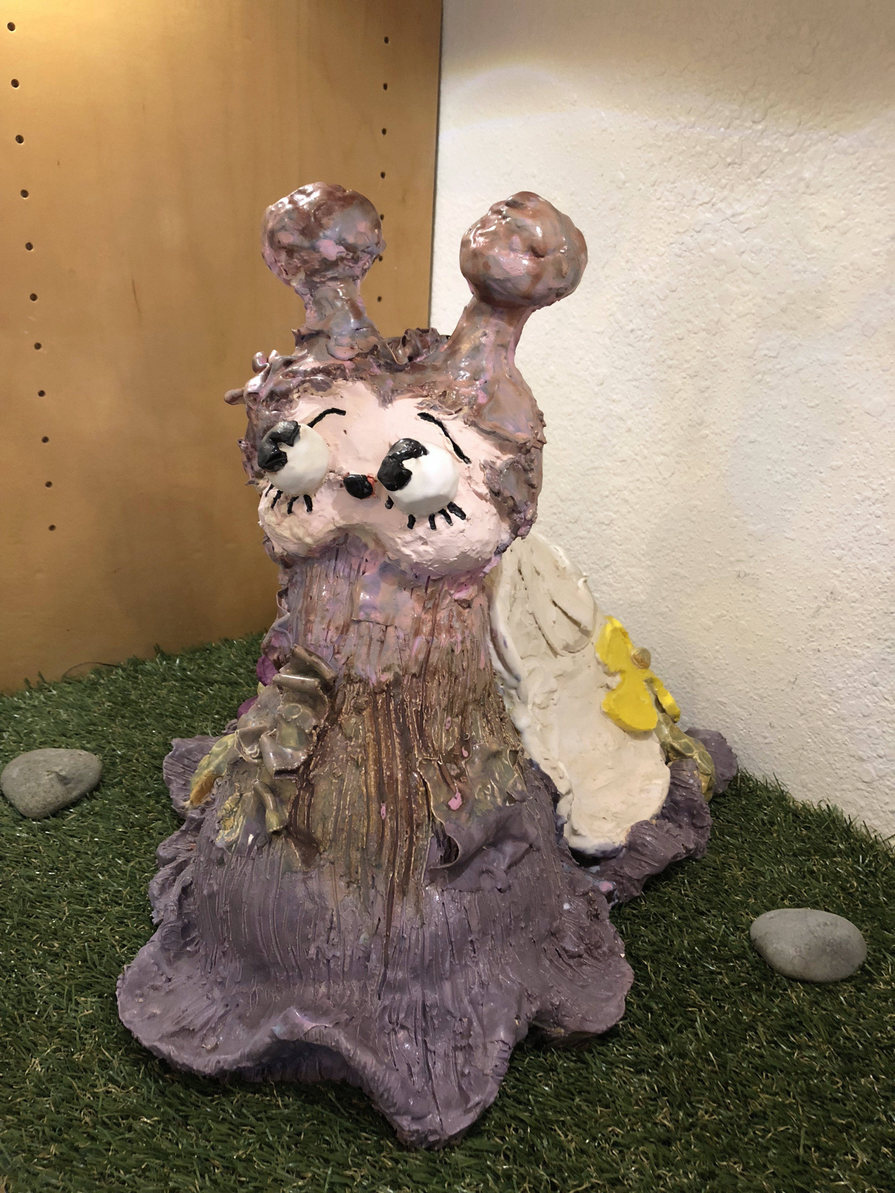 Frontal close up of a lavender ceramic snail scupture with carooty eyes